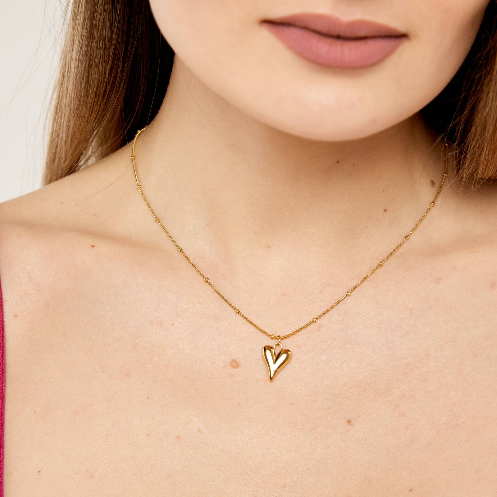 Woman wearing an 18k gold-plated stainless steel necklace with a heart-shaped pendant, smooth polished surface, and a snake chain design.